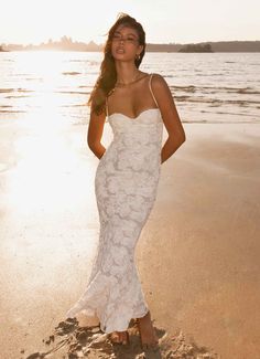 a woman standing on top of a beach next to the ocean wearing a white dress