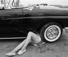 a woman sitting on the ground next to a parked car with her legs crossed out