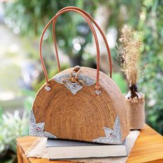 a brown purse sitting on top of a wooden table next to a book and plant