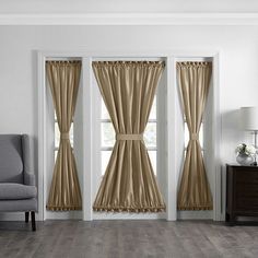 a living room with white walls and wooden floors, two windows covered in beige drapes