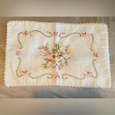 an embroidered placemat with flowers on it sitting on a white tablecloth covered surface