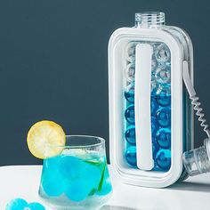 a glass filled with blue liquid next to an ice pack and lemon wedges on a table