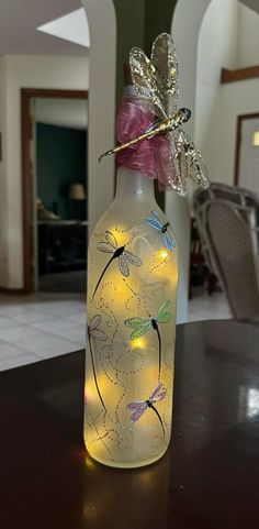 a lighted bottle with dragonflies on it sitting on a table in front of a doorway