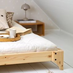 a bed with white sheets and pillows in a bedroom next to a table with two cups on it