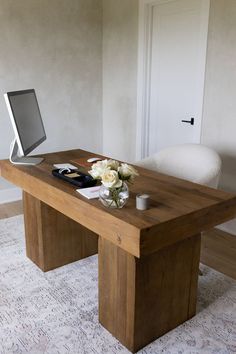 a wooden desk with a computer monitor and flowers on it