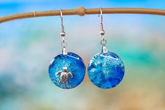 "Round asymmetric dangle earrings of the blue sea and a turtle in the sea. These coral reef effect earrings made with resin and with different shades of blue. Each piece of unique nautical jewelry is made with great delicacy and attention. Each earring is different, one representing the deep ocean and the other the beauty of a turtle in the sea. They are light and very original so they become the best gift. Each ocean round earrings is made with great finesse and no two are alike. So yours will Ocean-inspired Blue Earrings For Gifts, Blue Resin Earrings For Beach, Blue Resin Earrings For The Beach, Blue Round Pendant Earrings For Gift, Blue Round Pendant Earrings As Gift, Resin Drop Earrings For Beach, Ocean-inspired Blue Resin Jewelry, Blue Ocean-inspired Resin Jewelry, Blue Round Resin Jewelry