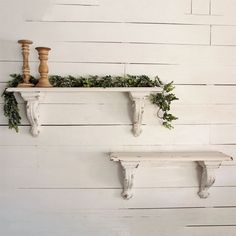 two white shelves with plants and candles on them against a white painted wall, one shelf is decorated with greenery