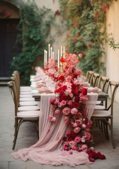 a long table with pink and red flowers on it is surrounded by chairs in front of an ivy covered wall