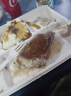 a plate with meat, mashed potatoes and gravy next to a coke