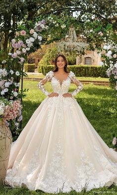 a woman in a wedding dress standing under an archway with flowers on the grass and greenery