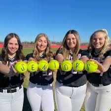 four girls in black and white baseball uniforms holding yellow balls