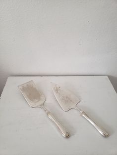 two silver spatulas sitting on top of a white counter next to each other