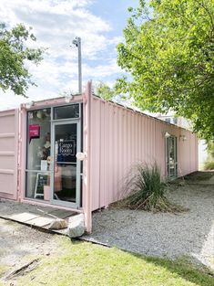 a pink shipping container sitting on top of a grass covered field next to a tree