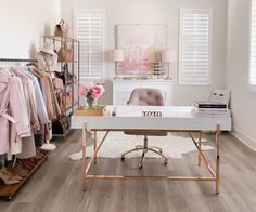 a room filled with lots of clothes on racks next to a desk and chair in front of a window