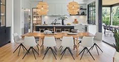 a dining room table with chairs and lights hanging from it's ceiling in front of an open kitchen