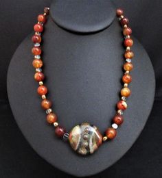 Artisan Statement Necklace~Brown Agate Statement Necklace~Carnelian Southwestern Necklace~Red Carnelian Chunky Necklace~ Handmade Necklace~ This 18" handmade artisan statement necklace features an iridescent artisan SRA focal bead . It is made with 10mm round polished carnelian beads and clear glass disc beads etched in gold.  The colors are a rich rust golden orange with earth tone greens, brown, gold and taupe. Because of its blend of colors, it is difficult to describe it although I think pic Artisan Czech Glass Necklaces With Natural Stones, Artisan Necklace With Czech Glass And Natural Stones, Artisan Necklace With Natural Stones And Czech Glass, Artisan Czech Glass Necklace With Natural Stones, Unique Orange Agate Necklace, Natural Stones Czech Glass Round Necklaces, Czech Glass Natural Stone Necklaces, Round Carnelian Necklaces With Natural Stones, Round Czech Glass Necklaces With Natural Stones