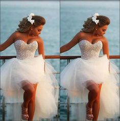 a woman in a white dress sitting on a railing next to the ocean with her legs crossed