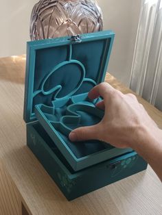 a person is opening the lid of a blue box on a table with an owl statue in the background