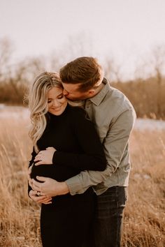 a pregnant couple cuddles in the tall grass