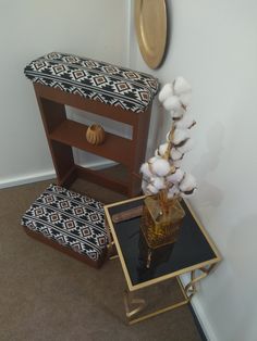 a vase with cotton flowers on a small table next to a stool and mirror in a room