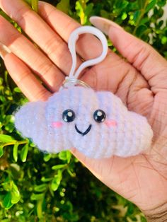 a hand holding a small keychain shaped like a cloud with a smiling face