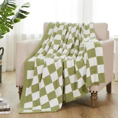 a green and white blanket sitting on top of a couch next to a potted plant