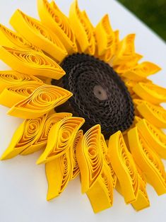 a sunflower made out of yellow paper sitting on top of a white table with grass in the background