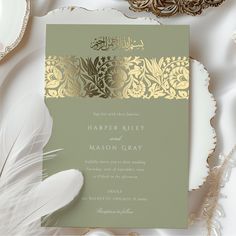 a wedding card with gold foil on it and a white feather laying next to it