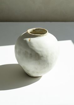 a white vase sitting on top of a table next to a shadow from the sun