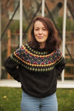 a woman standing in front of a building wearing a black sweater with colorful designs on it