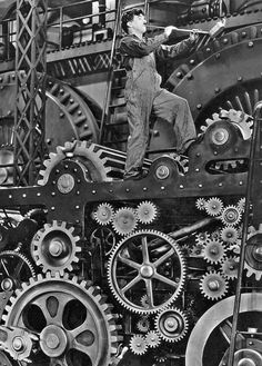 an old black and white photo of a man working on a large machine with gears