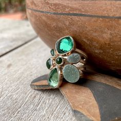 This sterling silver ring is perfect for the person who loves green semi-precious gemstones, and especially in different forms. The ring was made by one of the most beloved Albuquerque designers, Lilly Barrack, and it consists of a thick wire sterling silver band atop which sit seven smooth bezels, each with a green gemstone in a color palette that tends toward the forest-slash-emerald tones. There are two druzies, three opaque jade tone stones, and the two largest are faceted and display more clairty. With the thick sterling silver wraparound band and those various gemstones, the piece conjures images of forests and moss. The end result is a modernist and uncommon statement-cocktail ring. This ring was made when Barrack was a practicing artist, during the late 1990s to early 2000s. From h Green Multi-stone Emerald Rings, Green Stackable Rings With Accent Stones For May Birthstone, Fine Jewelry Green Oval Stackable Rings, Fine Jewelry Green Stackable Jewelry, Emerald Multi-stone Jewelry For May Birthstone, Fusion Style Green Rings With Accent Stones, Fine Green Stackable Jewelry, Green Fusion Style Rings With Accent Stones, Green Fusion Rings With Accent Stones