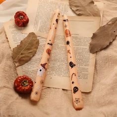 two wooden sticks with faces on them sitting next to an open book and some leaves