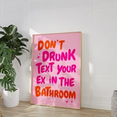 a pink sign that says don't drunk text your ex in the bathroom next to a potted plant