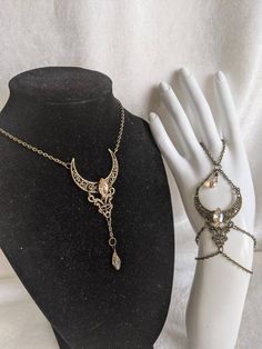 A beautiful and unique jewelry set which includes a pendant necklace and hand chain, featuring a filigree moon and connector charm with a crystal decorating the center of the moon and a drop crystal hanging from the pendant. Choose Crystal Shape between horse eye (as pictured) or teardrop (horse eye will be sent if unspecified) Choose necklace length from the diagram in the listing picture (14 inches plus 1.5 inch extension chain will be sent if unspecified) Crescent Moon Charm Jewelry For Parties, Crescent Moon Charm Party Jewelry, Metal Jewelry With Moon Charm For Party, Moon Charm Pendant Jewelry For Party, Party Pendant Jewelry With Moon Charm, Party Moon Charm Pendant Jewelry, Metal Moon Phase Jewelry For Parties, Mystical Sun And Moon Design Jewelry For Wedding, Fantasy Moon Shaped Jewelry Gift