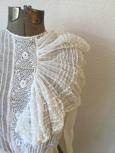 "Vintage Victorian white cotton net and lace blouse with long sleeves and a very large flouncy ruffle coming off a crochet placard down the front. The net has pintuck creating a ribbon effect The sleeves each have two functioning buttons and a small trim of lace. The waist is gathered to create a ruffle around and is backed with ribbon. The whole blouse is lined with net. The blouse buttons down the back with a covered placard to hide the buttons. Single hook and eye at waist. Simple crew neck. Fitted Cotton Lace Top With Ruffles, Vintage White Crochet Lace Top, White Lace Top With Ruffles, Long Sleeve Lace Top With Ruffles For Wedding, White Cotton Lace Top With Lace Trim, Vintage Lace Top With Ruffles, White Cotton Lace Top With Lace Collar, Wedding Long Sleeve Lace Top With Ruffles, Vintage White Tops With Crochet Lace