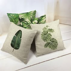 three pillows with green leaves on them sitting on a white wooden floor in front of a window