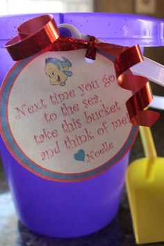 a purple bucket with a red bow on it and a message in the top that says next time you go to the sea take this bucket and think of me