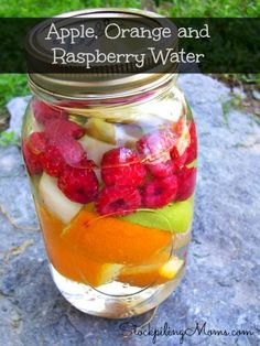 an apple, orange and raspberry water is in a mason jar on a rock