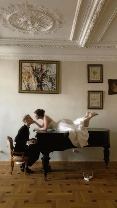 a man and woman sitting at a piano in a room with paintings on the wall