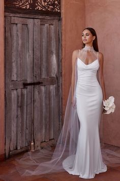 a woman in a white wedding dress with a veil on her head standing next to a wooden door