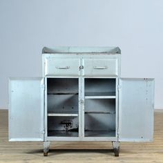 an old metal cabinet with two doors and shelves on wheels, sitting on a wooden floor