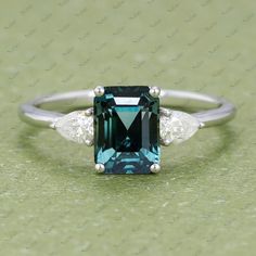 an emerald and diamond ring with three diamonds on the side, sitting on a green surface