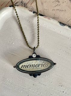 "Ronnie would never let go of her memories   The necklace features a mini shadow box pendant that encases the word \"Memories.\" The pendant has a vintage appearance and includes a small rhinestone for added detail and sparkle. The necklace itself is designed with a ball chain and measures 18\" in length. It is commonly worn closer to the neckline due to its shorter length. The necklace is secured with a lobster clasp, which is a popular type of closure in jewelry. This necklace offers a sentime Vintage Charm Necklace For Anniversary, Vintage Pendant Necklace For Anniversary Gift, Antique Keepsake Necklaces With Charms, Vintage Engraved Charm Necklaces As Keepsakes, Vintage Engraved Charm Necklaces For Keepsake, Vintage Charm Necklaces For Anniversary, Vintage Charm Necklaces For Anniversary Gift, Antique Necklaces With Vintage Charm For Anniversary, Antique Charms Necklaces For Memorials