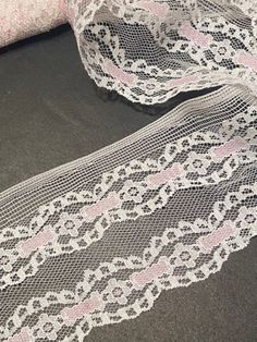 white lace with pink flowers on it sitting on top of a black surface next to a piece of cloth