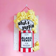 a sign that says what's poppin next to some popcorn on a pink background