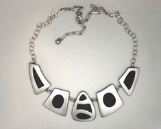 "This completely hand made silver statement necklace has 5 separate pieces linked together. Each piece has a different geometric silver design that frames a filling of black crushed stone that's flush with its frame. This piece has a \"WOW\" factor.  The 5 pieces have a light satin finish and measure 6\" across with the central piece being 1-1/4\" long.  The 5 pieces are extended with a combination of round cable chain and 4x10 pulled cable chain on each side making the length 18\" with a 2\" ex Unique Design Black Metal Jewelry, Black Metal Jewelry With Unique Design, Contemporary Black Jewelry With Oxidized Finish, Artisan Sterling Silver Nickel-free Necklace, Nickel-free Multi-strand Metal Necklaces, Artistic Sterling Silver Nickel-free Necklace, Artistic Multicolor Nickel-free Necklace, Luxury Modernist Sterling Silver Necklace, Silver Statement Necklace