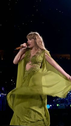 a woman in a green dress holding a microphone and singing on stage with lights behind her