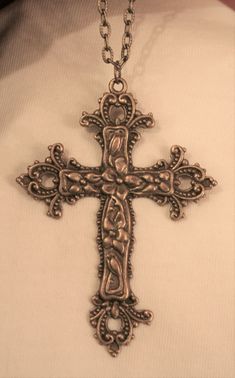 This goldtone necklace features a mid-to-large-sized pectoral cross pendant with swirled metal beaded fleur de lis accents on the ends of the arms.  The body shines with dogwood flowers - a symbol of new and everlasting life.  The reverse has a shiny finish and it measures 2 1/8 inches wide and 3 inches long.  The chain is 24 inches and closes with a safety catch Ornate Cross Necklace With Intricate Design, Bronze Cross Bohemian Necklace, Vintage Metal Cross Pendant Necklace, Bronze Bohemian Cross Necklace, Bohemian Bronze Cross Necklace, Vintage Metal Crucifix Cross Necklace, Antique Bronze Cross Necklace, Antique Cross Necklace With Large Pendant, Antique Metal Cross Necklace