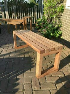 a wooden bench sitting on top of a brick patio next to a garden table and chairs